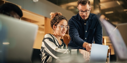 A man and a woman looking at work on a laptop together