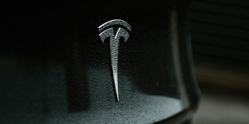 A rain-flecked Tesla badge on a grey car