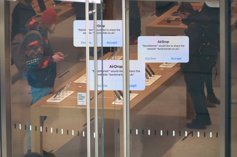 AirDrop messages promoting BackMarket, superimposed on top of an image of customers in an Apple Store