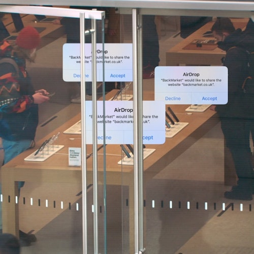 AirDrop messages promoting BackMarket, superimposed on top of an image of customers in an Apple Store