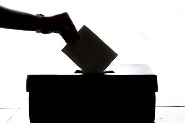 A hand places a voting paper into a ballot box