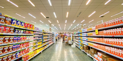 Supermarket aisles showing colourful goods on shelves, with a trolley in the distance