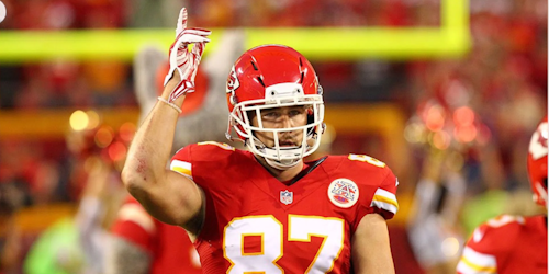 Travis Kelce in Kansas City Chiefs red uniform raising a finger to the sky